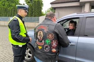 Zdjęcie przedstawia policjanta oraz motocyklistę przekazujących naklejkę kierowcy.