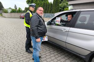 Zdjęcie przedstawia policjanta oraz motocyklistę przekazujących naklejkę kierowcy.