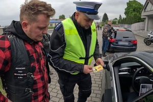 Zdjęcie przedstawia policjanta oraz motocyklistę przekazujących naklejkę kierowcy.