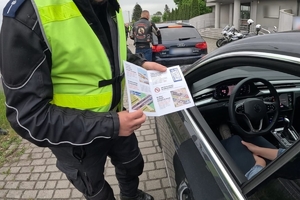 Zdjęcie przedstawia policjanta trzymającego w dłoniach rozłożoną ulotkę.