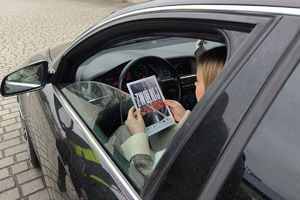 Zdjęcie przedstawia kobietę za kierownicą pojazdu, która trzyma w dłoniach rozłożoną ulotkę.