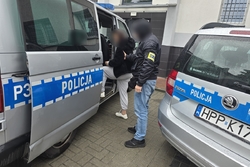 Zdjęcie przedstawia nieumundurowanego policjanta, który wprowadza zatrzymaną do radiowozu.