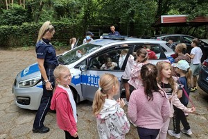 Zdjęcie przedstawia policjantkę, policjanta, radiowóz oraz dzieci wsiadające do niego.