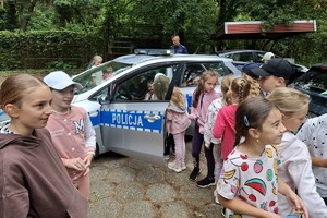 Zdjęcie przedstawia policjanta, radiowóz oraz dzieci wsiadające do niego.