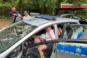 Zdjęcie przedstawia policjanta, radiowóz oraz dzieci wsiadające do niego.