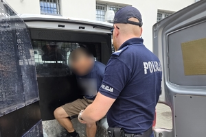 Zdjęcie przedstawia policjanta wyprowadzającego zatrzymanego z radiowozu.