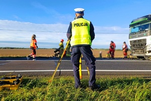 umundurowany policjant stoi tyłem, prowadzi oględziny w tle ratownicy medyczni i strażacy