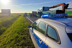 radiowóz policyjny, obok ciężarówka biorąca udział w wypadku, dalej stoją policjanci, ratownicy oraz karetki pogotowia