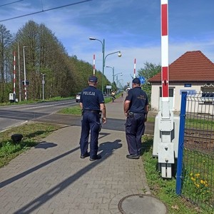na zdjęciu widoczni są umundurowany policjant i strażnik ochrony kolei stojący przy przejeździe kolejowym