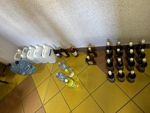 na zdjęciu widoczne są  stojące na posadce plastikowe pojemniki 5 litrowe ze spirytusem oraz butelki z alkoholem