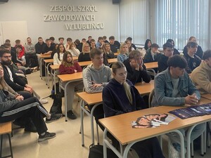 uczniowie siedzący przy ławka na dużej sali lekcyjnej