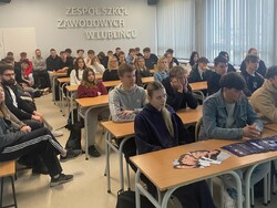 uczniowie siedzący przy ławka na dużej sali lekcyjnej