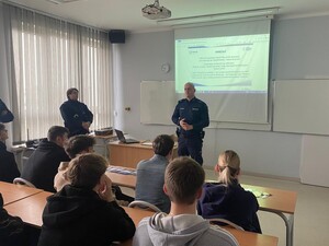 policjant stoi n a środku sali przed siedzącymi za ławkami uczniami