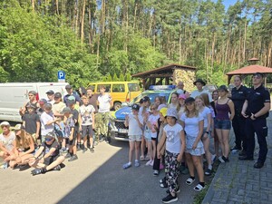 radiowóz grupa dzieci wokół niego obok dwoje policjantów