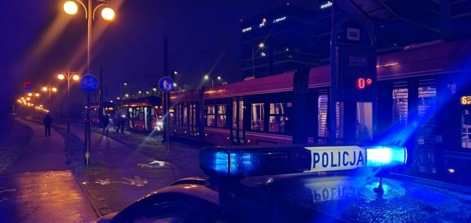 zdjęcie kolorowe: na pierwszym planie policyjny radiowóz, a w tle przystanek tramwajowy i tramwaj z uszkodzonym wagonem