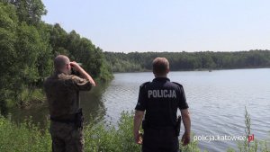 Policjant i funkcjonariusz Straży Leśnej obserwują przez lornetkę teren