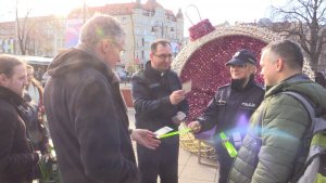 Policjanci wraz z księdzem wręczają pieszym elementy odblasko