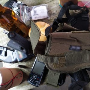 zdjęcie kolorowe stołu na którym znajduje się butelka po piwie, torba typu nerka, telefon komórkowy, materiały pirotechniczne, paralizator, bułka