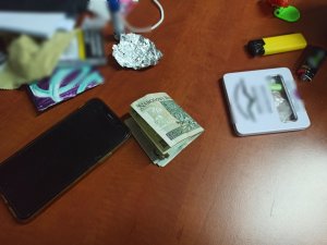 zdjęcie kolorowe: telefon komórkowy, folia aluminiowa, banknoty, metalowe pudełko z narkotykami ułożone na stole