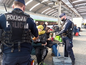 zdjęcie kolorowe: policjanci katowickiego oddziału prewencji rozdający jedzenie dzieciom oczekującym na peronie kolejowym
