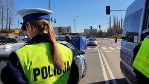 zdjęcie kolorowe: policjantka wydziału ruchu drogowego stojąca przy radiowozie na miejscu śmiertelnego potracenia kobiety