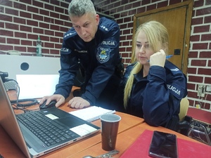 zdjęcie kolorowe: policjant i policjantka w mundurach ćwiczebnych stojący przed komputerem na stanowisku dowodzenia
