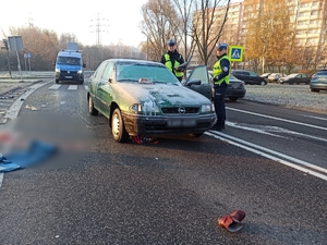 zdjęcie kolorowe: policjanci ruchu drogowego wykonujący oględziny samochodu którym potrącono kobietę na oznakowanym przejściu dla pieszych