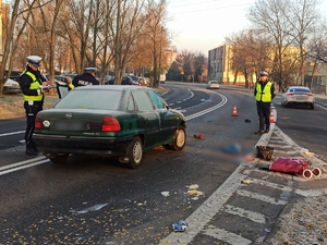 zdjęcie kolorowe: trzech policjantów ruchu drogowego wykonujący oględziny samochodu którym potrącono kobietę na oznakowanym przejściu dla pieszych