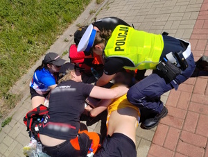 zdjęcie kolorowe: policjantka ruchu drogowego i ratownicy medyczni udzielający pomocy biegaczowi, który zasłabł