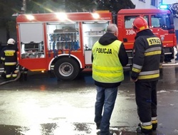zdjęcie kolorowe: policjant i strażak stojący przed wozem strażackim