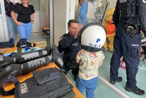 zdjęcie kolorowe przedstawiające policjanta, który pomaga założyć chłopcu na głowę, kask który używa podczas służby