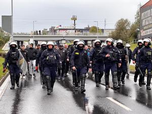 zdjęcie kolorowe: policjanci oddziału prewencji zabezpieczający przemarsz kibiców na mecz piłki nożnej rozegrany pomiędzy drużynami GKS-u Katowice i Pogoni Szczecin