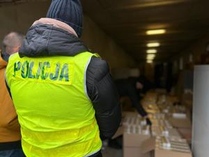 Na zdjęciu policjant w kamizelce a za nim zatrzymane nielegalne papierosy