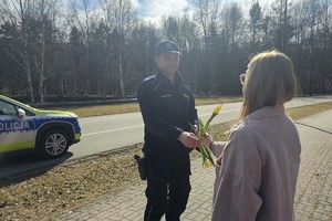 Na zdjęciu policjant wręczający kwiaty kobiecie