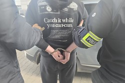 Na zdjeciu widoczny zatrzymany z założonymi kajdankami oraz dwaj nieumundurowani policjanci jeden z opaską Policja na ramieniu