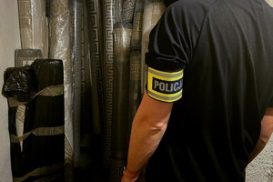 Na zdjęciu policjant z opaską na ramieniu Policja a przed nim dywany