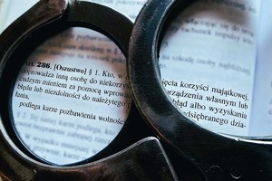 Na zdjęciu policyjne kajdanki i kodeks karny, artykuł 286 oszustwo