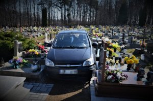samochód osobowy koloru granatowego w alejce cmentarza