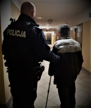 umundurowany policjant prowadzi starszego mężczyznę korytarzem izby zatrzymań