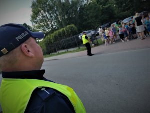 umundurowany policjant stoi na chodniku, w tle widać ustawione w szeregu dzieci