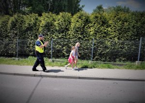 chodnikiem idą dzieci oraz policjant w odblaskowej kamizelce