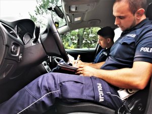 policjanci drogówki siedzą w radiowozie i wypisują dokumentację