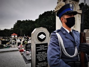 policjant w asyście honorowej na cmentarzu w Ornontowicach. W tle fragment pomnika ku czci poległych policjantów II RP