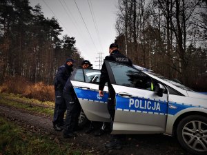 policjanci wraz z zatrzymanym wsiadają do oznakowanego samochodu, zaparkowanego w lesie