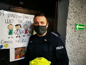 dzielnicowy na spotkaniu z obywatelami Ukrainy, za nim drzwi, a na nich plakat dla dzieci