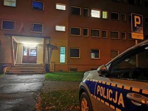 zdjęcie kolorowe: widać fragment policyjnego radiowozu oraz fragment budynku mikołowskiej komendy. Zdjęcie zrobione w porze wieczornej