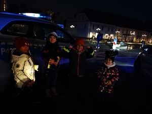 na zdjęciu widać grupę małych dzieci, którzy stoją przed policyjnym radiowozem