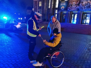 na zdjęciu widać policjanta drogówki, który przekazuje odblask chłopcu na wózku inwalidzkim