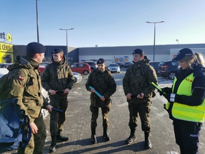 na zdjęciu widać stojących obok siebie, na parkingu przy centrum handlowym, policjantów i uczniów klasy mundurowej
