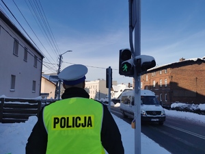 zdjęcie przedstawia policjanta przechodzącego przez przejście, w tle sygnalizator wskazuje światło zielone